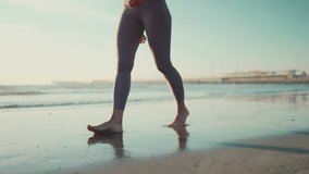 Close up shot of woman wearing leggings walking along the sea. Close up female legs on the beach