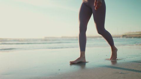 Close up shot of woman wearing leggings walking along the sea. Close up female legs on the beach