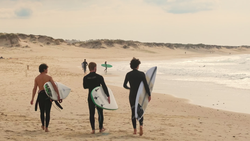 Unidentified surfers with surf board walk on the Baleal beach and watching other surfers catching waves. Baleal is a popular surfing spot in Portugal.  Royalty-Free Stock Footage #1091386845