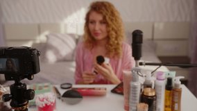 Curly girl blogger records a video about skin care cosmetics in her bedroom