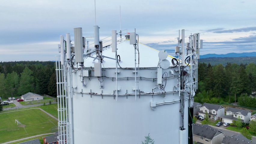 Close up aerial shot of the many pieces of telecommunication equipment on top of a water tower.