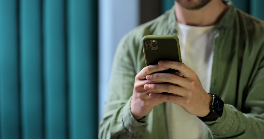 Portrait of a man in glases with smartphone in the hands, browsing something at the cafe. Man is using smartphone for messaging, texting.