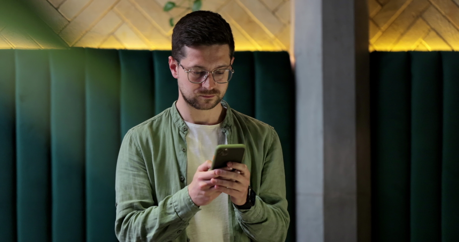 Handsome man using smartphone in Cafe. Male in glases smiling, checking social media and typing message.