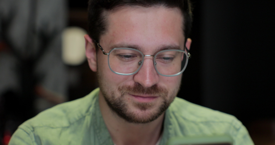 Handsome man using smartphone in Cafe. Male in glases smiling, checking social media and typing message.