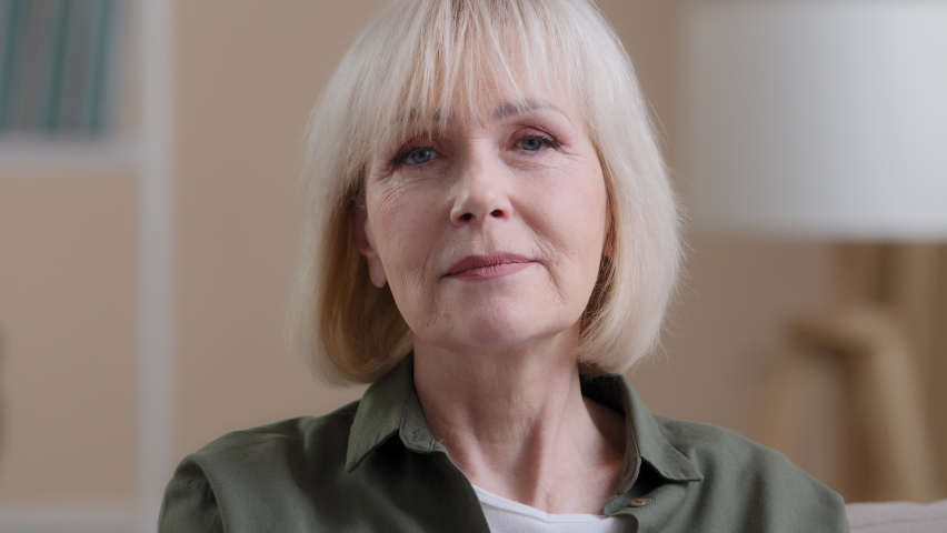 Close-up portrait old caucasian 60s woman elderly lady grandmother zipping lips locking mouth imitates throwing away key keep secret mystery silence gesture secrecy information stop talking gesture