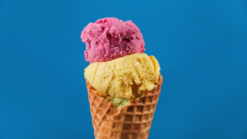 Colorful ice cream in waffle cone rotating on blue background. Close-up of sweet dessert. Delicious pink, yellow and green ice cream. Ice cream like traffic lights. 4K, UHD Royalty-Free Stock Footage #1091406371