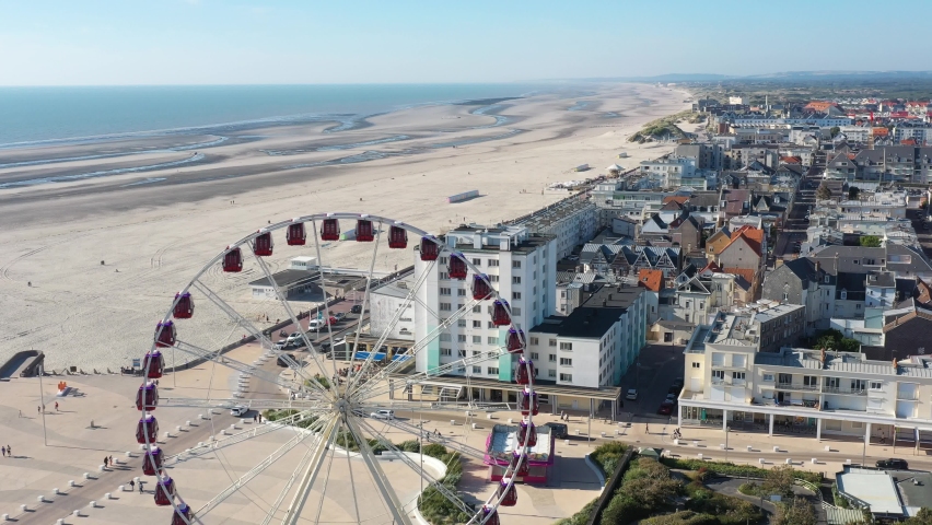 France, Nord Pas-de-Calais, Berck, drone aerial view above the big ferris wheel facing Manche sea and beach in the downtown. Low tide during summer with a blue sky and turquoise sea.