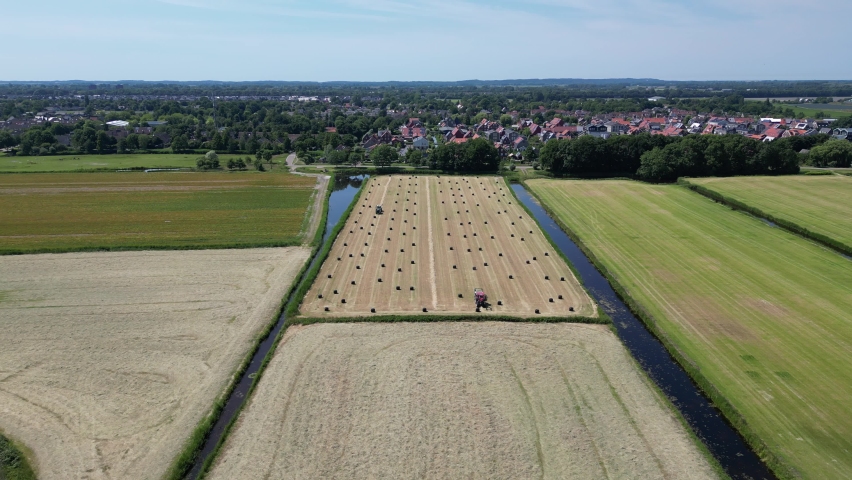 Farmers gathering hay bales from the land with tractors