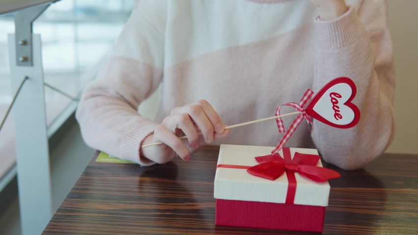 Young woman holding heart shaped decor stick with gift box. Girl is waiting for her boyfriend in restaurant. Holiday and date concept of Valentine's Day, women's day, Mother's day, 8 March, Birthday Royalty-Free Stock Footage #1091414927