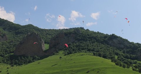Paragliding pilots fly paragliders among clouds and green mountains.