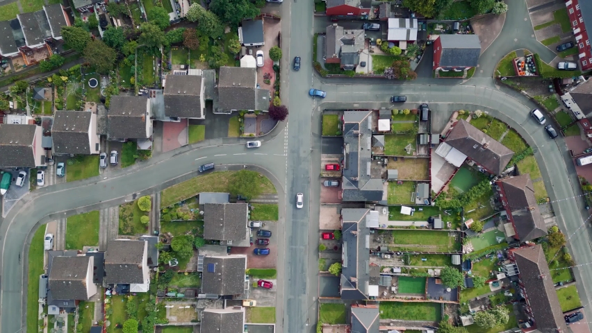 Aerial drone lifestyle concept flying over a street lined with British terraced houses during the golden hour as the sun is setting. Following a blue car along the road, past shops and people walking. Royalty-Free Stock Footage #1091416731