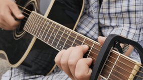 a teenager plays an acoustic guitar, rearranging the chords on the strings and fixing the capadastr on the neck of the guitar, raising the tonality of the music by one tone. Slow motion, close up