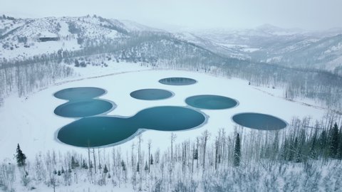 Aerial view of idyllic winter vacation destination with beautiful natural environment. Astonishing landscape with circular ponds and fir forest around as seen from above. High quality 4k footage