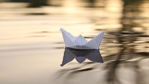 A paper boat is floating on the waves in the water at a beautiful sunset. Origami ship Sailing. The concept of a dream, future, childhood, freedom or hope. Slow motion. High quality FullHD footage
