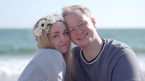 Man hugging his wife in a beautiful flower crown on a sunny summer day. Portrait of lovely couple smiling on a sandy beach along ocean coastline. High quality 4k footage