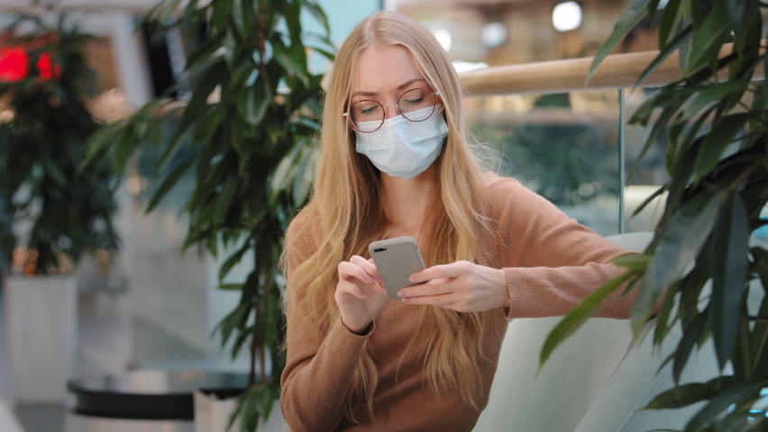 Displeased blonde Caucasian woman in medical mask looking at smartphone screen dissatisfied with bad news message spam scam negative sms app problem. Unhappy stressed sad female lost with smartphone Royalty-Free Stock Footage #1091426301
