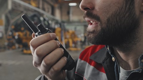 Close-up of cropped bearded male technician talking into walkie talkie at factory in afternoon