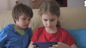 Boy and Girl Plays Video Game Smartphone on Sofa Friends Using Phone for Gaming Online Education Social Media. Children Playing Games In Phone at Home on Couch. Kids Playing Video Game on Mobile Phone