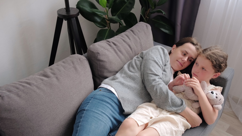 Loving young mother cuddles little daughter, family lying on comfy sofa in living room, feel unconditional love show devotion, express caress. Caring mom, adopted kid, Mothers Day celebration concept Royalty-Free Stock Footage #1091431747