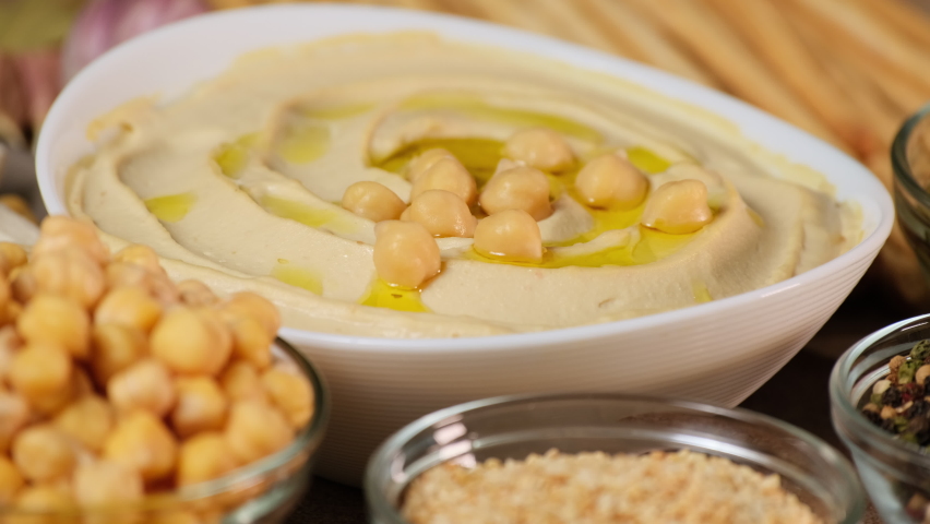 Chickpea hummus made from mashed chickpeas dip with tahini lemon garlic and olive oil close-up. Enjoying yummy hummus with pita, lavash, bread sticks, grissini. Kosher healthy vegan food. Lean dish Royalty-Free Stock Footage #1091433381