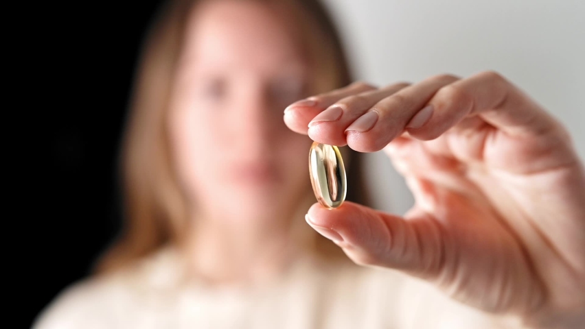 Young attractive girl shows golden capsule Omega 3 vitamin d in hand and then puts it in her mouth. Vitamins, pills, Supplements, pharmaceutical theme, healthy lifestyle, medicine. Fish oil pill