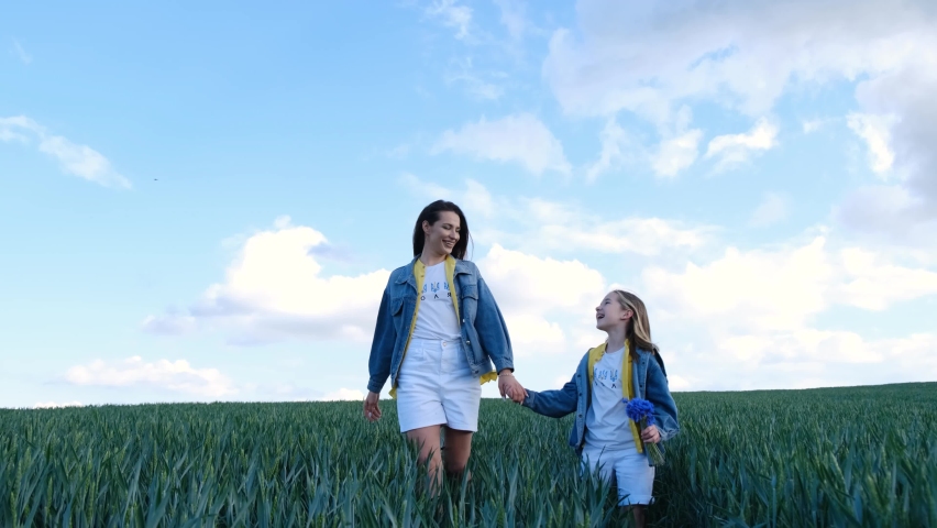 Mom and daughter walk in a green field of young wheat. Children run on the green fresh grass