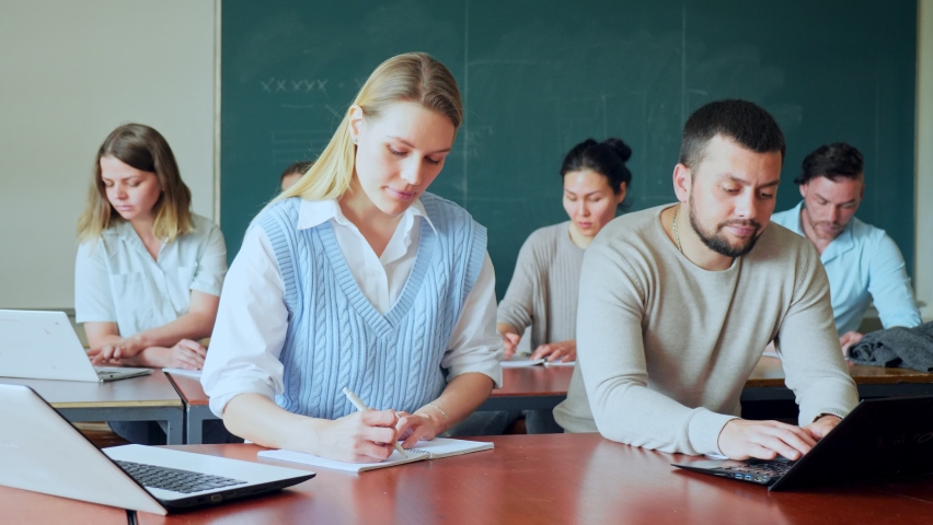 Group of adult students sitting at table in classroom, man exercising with laptop. | Shutterstock HD Video #1091434671