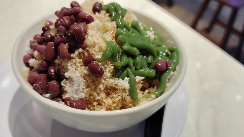 Close-up view of the cendol dessert with gula Melaka syrup. Cendol is made from crushed ice cubes, jelly, coconut milk, and red beans. Royalty-Free Stock Footage #1091435697