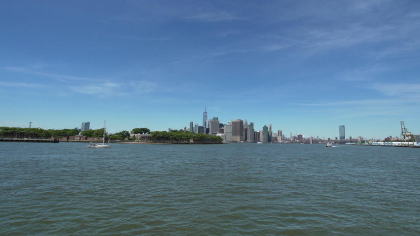 Sailing by NYC ferry, green Governors island is on the left, view of Manhattan and its skyscrapers. Ferry arrives to The Atlantic Dock (also called the Atlantic Basin). Summertime | Shutterstock HD Video #1091439625
