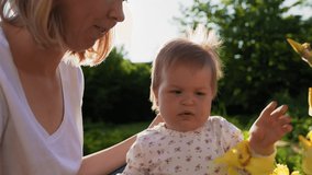 Children's autism. Smiling mother and her baby daughter touches the yellow iris flowers in the garden. Slow motion. Summer park in the background.