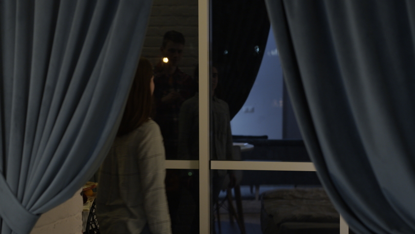 young guy tenderly hugs his beloved who stands by the window and admires the view of the evening city