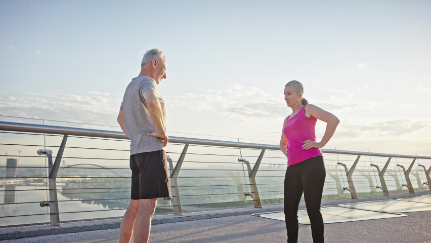 Pensioners do pelvic rotation exercise standing at viewpoint overlooking river and city. Active man and woman lead healthy life in morning slow motion Royalty-Free Stock Footage #1091447911