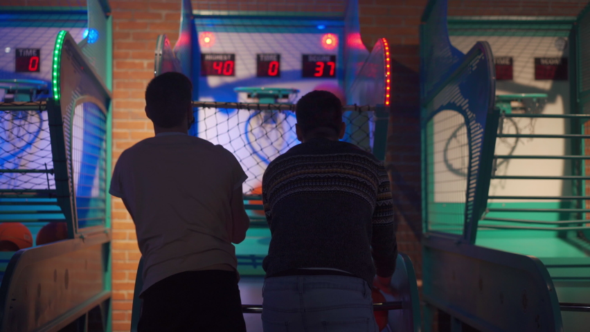 People back view Playing Basketball and Throwing Ball at Arcade Machine in Game Zone Amusement centre in Shopping mall. Two unrecognizable person have fun playing arcade machine Royalty-Free Stock Footage #1091449599