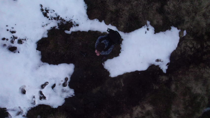 Playful birdeye shot of a hiker drawing back an imaginary bow and firing the drone up like an arrow revealing a snowy foggy mountain