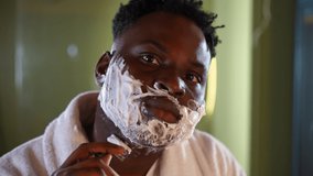 Headshot of concentrated man shaving stubble with razor looking at camera. Close-up front view of focused African American young guy doing morning routine in bathroom at home indoors - Powered by Shutterstock - Get 15% off with code: PIKWIZARD15