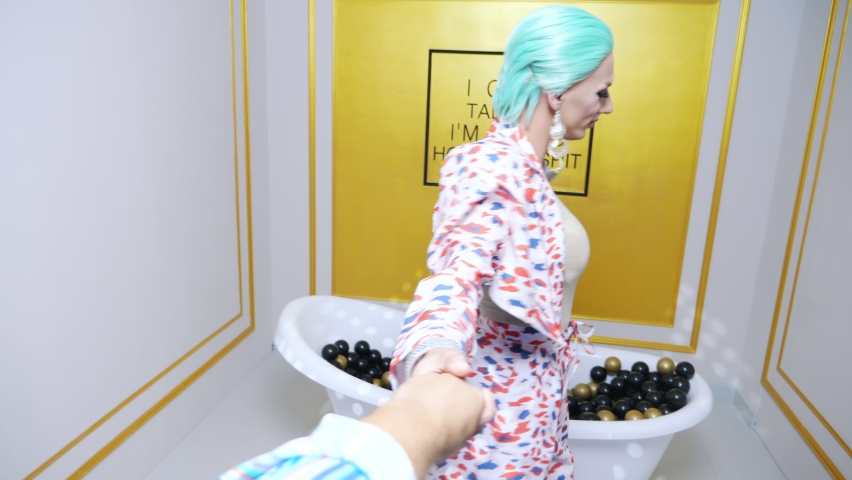 A handsome transgender guy in a blue wig and makeup leads a man by the hand to a bathroom with plastic balls. first-person view. | Shutterstock HD Video #1091456777