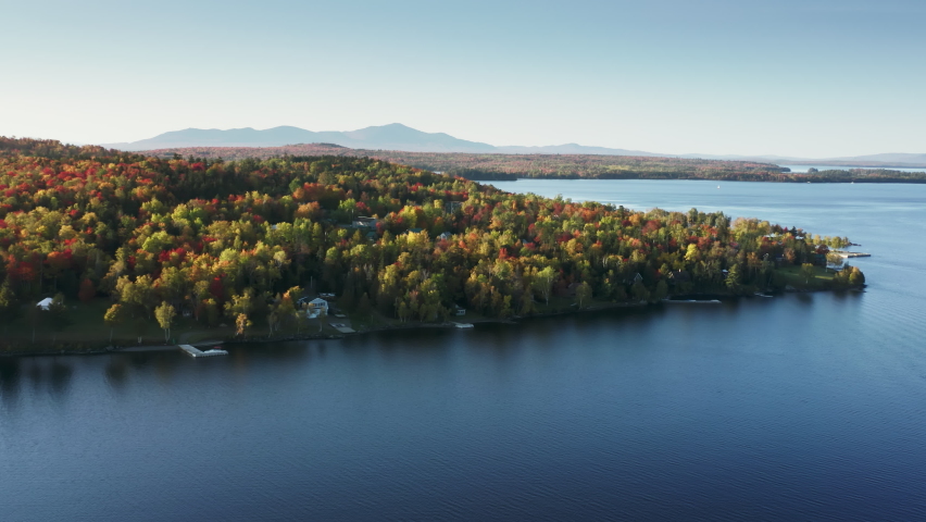 Deep blue still water in autumn forest lake with foliage trees. Aerial view of blue lake at colorful forests. View on Moosehead Lake at fall woodland forest Maine. Over crystal clear fresh lake water