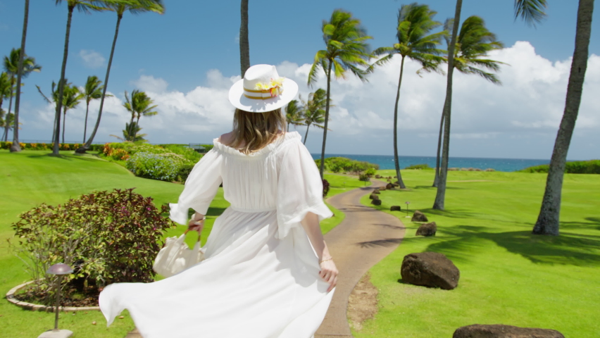 Happy traveler blogger adores summer vacation on Hawaii island RED shot. Slow motion elegant lady happily walking by tropical island on sunny summer day. Woman enjoying palm trees and ocean landscape Royalty-Free Stock Footage #1091457395