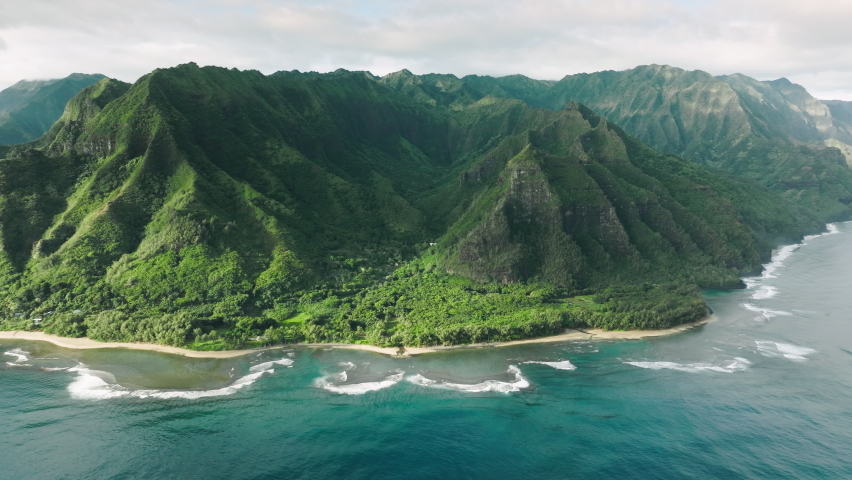 Breathtaking teal blue ocean waves at high green peaks formations with steep green summits. Panoramic aerial of scenic tropical Hawaii nature. Cinematic green mountain landscape of wild island nature Royalty-Free Stock Footage #1091457399
