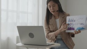 Young asian business woman using laptop computer for video conference online, businesswoman working with video call for meeting and showing graph report for finance, communication concept.