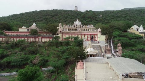 Palitana , Gujarat , India - 06 14 2022: Aerial forward drone shot of the Palitana temple surrounded with temple and trees. Some of the intricately carved marble shrines making up the vast temple complex