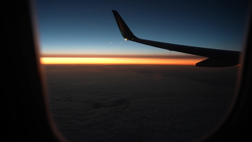 Looking out of window of flying in darkness airplane. Point of view 4k video footage of amazing scenery during flight. Beautiful sunrise or sunset orange and blue sky outside of passanger air jet | Shutterstock HD Video #1091469605
