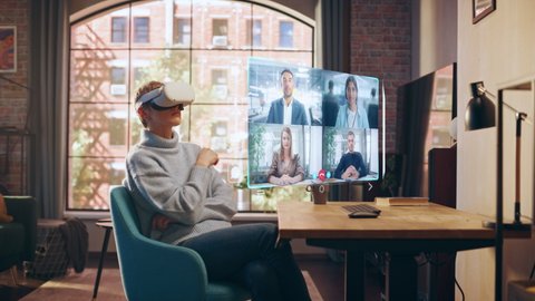 Successful Businesswoman Working from Home Living Room, Using Virtual Reality Headset to Participate in a Video Call Conference with Project Management Team. Young Female Talking with Colleagues.