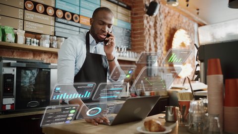 African American Coffee Shop Owner is Working on Computer and Talking on a Phone in a Cozy Cafe. Augmented Reality Icons Popping Out of Restaurant Manager's Laptop: Small Business Concept.