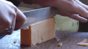 A 4K slow motion video of cheese being sliced at home in preparation for a melted cheese sandwich for lunch time. sliced on a grain end chopping block.