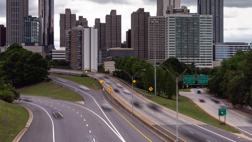 Panning out timelapse of downtown Atlanta from Jackson Street bridge overlooking the highway with motion blur on the vehicular traffic traveling on the roadway below and heavy cloud cover above.