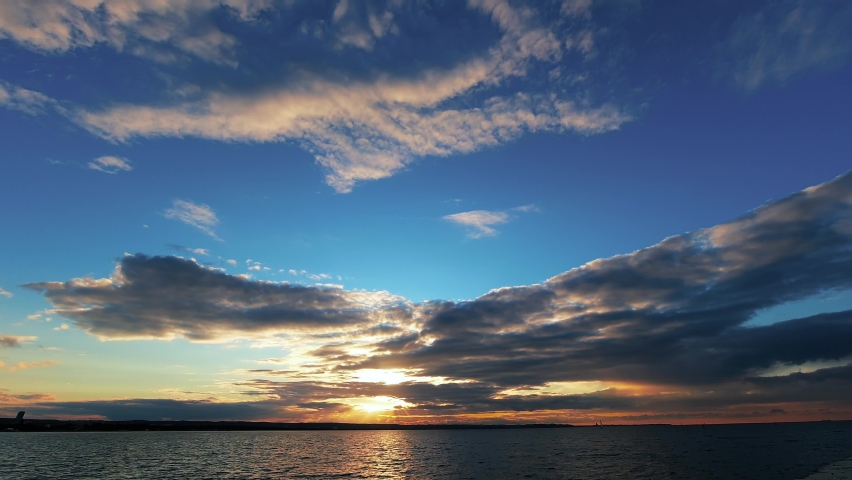 Beach sunset time lapse. Clouds fast in the sky. Time lapse of fast flying clouds in the sky. Big sun sets behind the clouds and the horizon. Beautiful sunset with clouds and sea with beach.