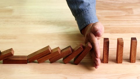 Business crisis, risk management concept. Businessman hand stopping or preventing falling dominos effect of risk, business crisis on wooden table, slow motion