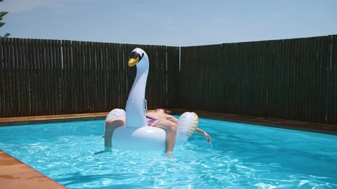 Young happy boy relaxes and sunbathe on inflatable swan toy in blue pool.