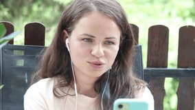 Smiling woman calling video using her smartphone and headphones.